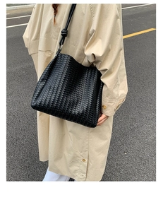 Detail of black woven shoulder bag with knotted strap on a casual trench coat outfit