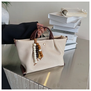 Detail of cream canvas tote bag with brown leather handles and wooden bead tassel charm