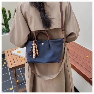 Detail of canvas handbag with brown leather straps and decorative wooden bead charm