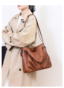 Close-up of vintage brown PU leather shoulder bag with textured finish on beige coat