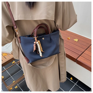 Detail of navy blue canvas tote bag with textured brown leather handles and bead charm
