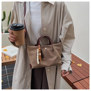 Detail of canvas handbag with brown handles and a decorative wooden bead charm