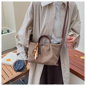 Detailed shot of brown canvas handbag featuring decorative wooden bead tassels and leather strap