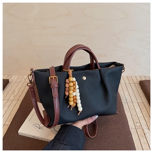 Detail of black canvas tote bag with brown leather handles and ethnic beaded charm