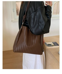 Macro detail of the woven dark brown leather texture on a spacious tote shoulder bag