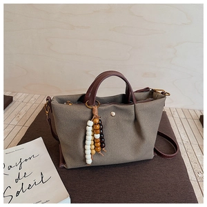 Detail of canvas handbag with brown leather trim and colorful bead tassel charm