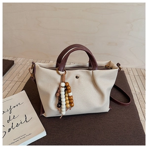 Detail of canvas tote bag with brown leather trim and decorative beaded tassel pendant
