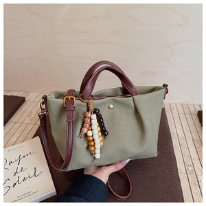 Detail of dark green canvas tote featuring brown leather handles and ethnic beaded tassel