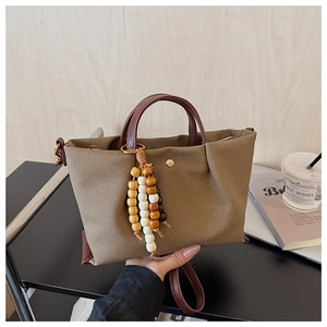 Detail of khaki canvas tote bag with brown leather handles and decorative wood bead tassels