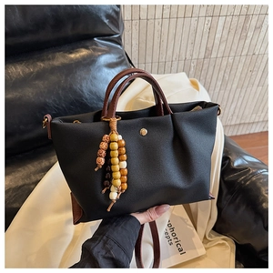 Detail of black nylon tote with leather handles and colorful beaded tassel charm