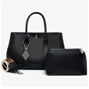 Detail of black litchi grain leather tote set with wide canvas strap and silver charm