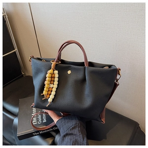 Detail of black canvas tote bag on leather seat with brown straps and beaded tassel