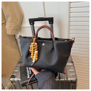 Detail of black canvas tote bag with brown leather handles and wooden bead charm on a suitcase