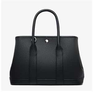 Detail of black pebbled leather tote bag with silver snap closure and round handles