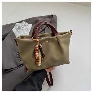 Close-up of olive canvas handbag featuring leather trim and colorful beaded charm