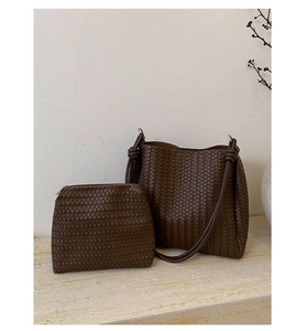 Detail of dark brown woven bucket bag and matching pouch on a minimalist stone surface