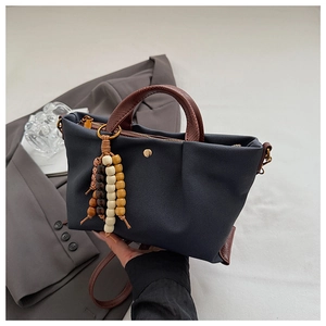 Detail of dark blue canvas handbag with brown leather straps and wooden bead charm