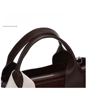 Close-up of leather handle and suede texture of a dark brown tote bag with wide strap