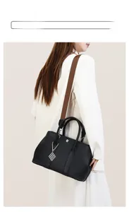 Close-up of black lychee leather tote bag featuring a brown woven strap and silver charm
