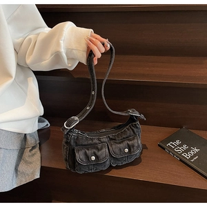 Detail of black denim motorcycle bag with dual flap pockets and metal hardware on wood