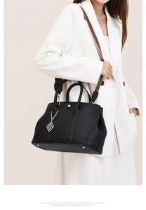 Detail of black pebbled leather tote bag with wide brown strap and silver pendant