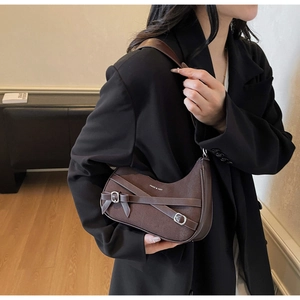 Détail du sac à bandoulière vintage marron avec boucles sur un blazer noir