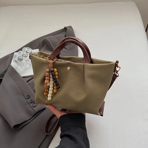 Olive green canvas handbag with brown leather trim and colorful beaded pendant
