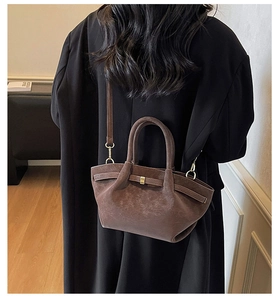 Detail of dark brown matte suede shoulder bag with gold buckle on a female model