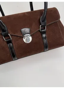 Close-up of brown suede handbag with black leather straps and silver metal clasp