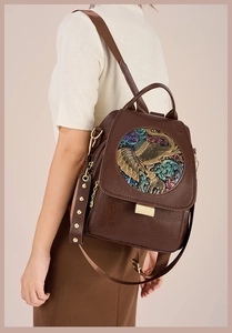 Detail of dark brown leather backpack featuring a vintage embossed elephant and floral plate