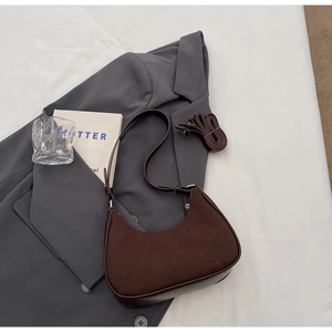 Détail du sac hobo en daim marron mat sur un costume gris avec bandoulière en cuir