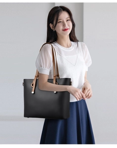 Close-up of black tote bag with brown handles and litchi grain texture on model