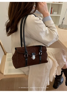 Detail of dark brown suede shoulder bag showing silver clasp and white stitching accents