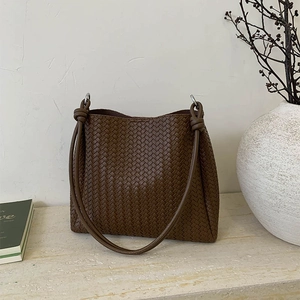 Brown woven bucket bag with knotted shoulder strap and large capacity in a minimalist setting