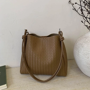 Brown woven leather bucket bag with large capacity on a minimalist stone background