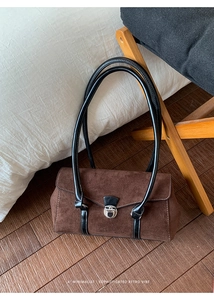 Detailed macro view of dark brown suede shoulder bag with silver turn-lock and black handle