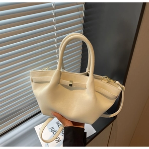 Detail of cream-colored winged handbag with gold buckles and detachable strap