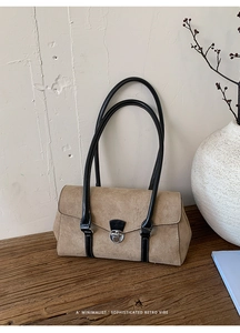 Detail view of khaki suede baguette bag with black leather straps on a wooden surface