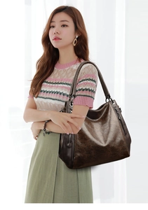 Detail of a large dark brown tote bag in glossy leather texture with side zipper accents