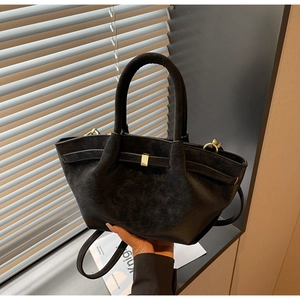 Detail of black matte wing bag with gold buckle and smooth leather texture finish