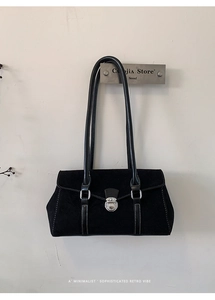 Detail of black suede shoulder bag with white contrast stitching and silver metal lock