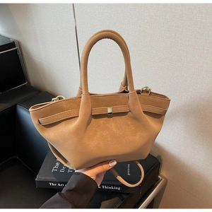 Detail of light brown matte leather wing bag with metal buckle and cylindrical handle