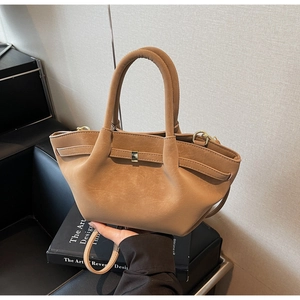 Detail of a matte tan pleated wing bag with golden metal buckle and smooth top handle