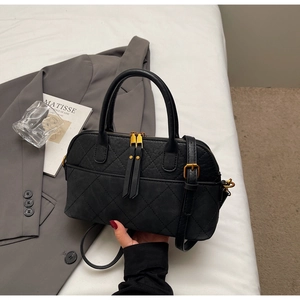 Close-up of black quilted shell bag with vintage gold hardware on a minimalist background