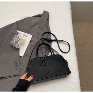 Détail du sac matelassé noir avec doubles poignées, zips en laiton et pieds métalliques
