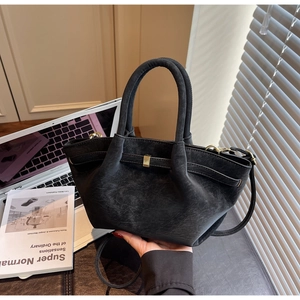 Close-up of black matte winged handbag with gold metal clasp on an office desk