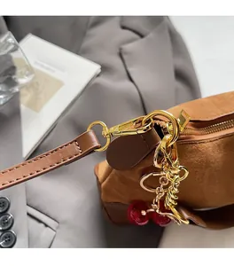 Detail van bruine suède handtas met gouden hardware en een decoratieve kersenhanger