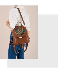 Close-up of brown leather backpack with golden buckle and circular dragon totem detail