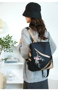 Detailed view of women's black backpack with pink floral embroidery on adjustable straps