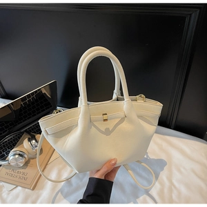 Side view of cream trapezoid leather bag with gold buckle on a white desktop
